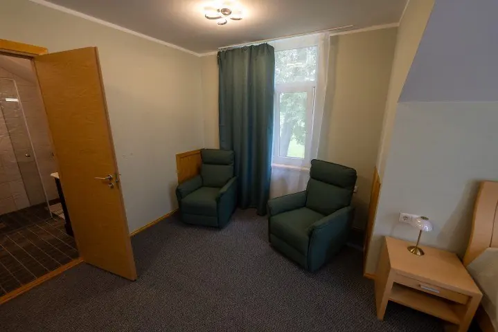 Host house room with two green armchairs and a bedside table