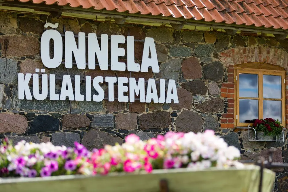 Sign ÕNNELA KÜLALISTEMAJA on a stone wall and a flower cart